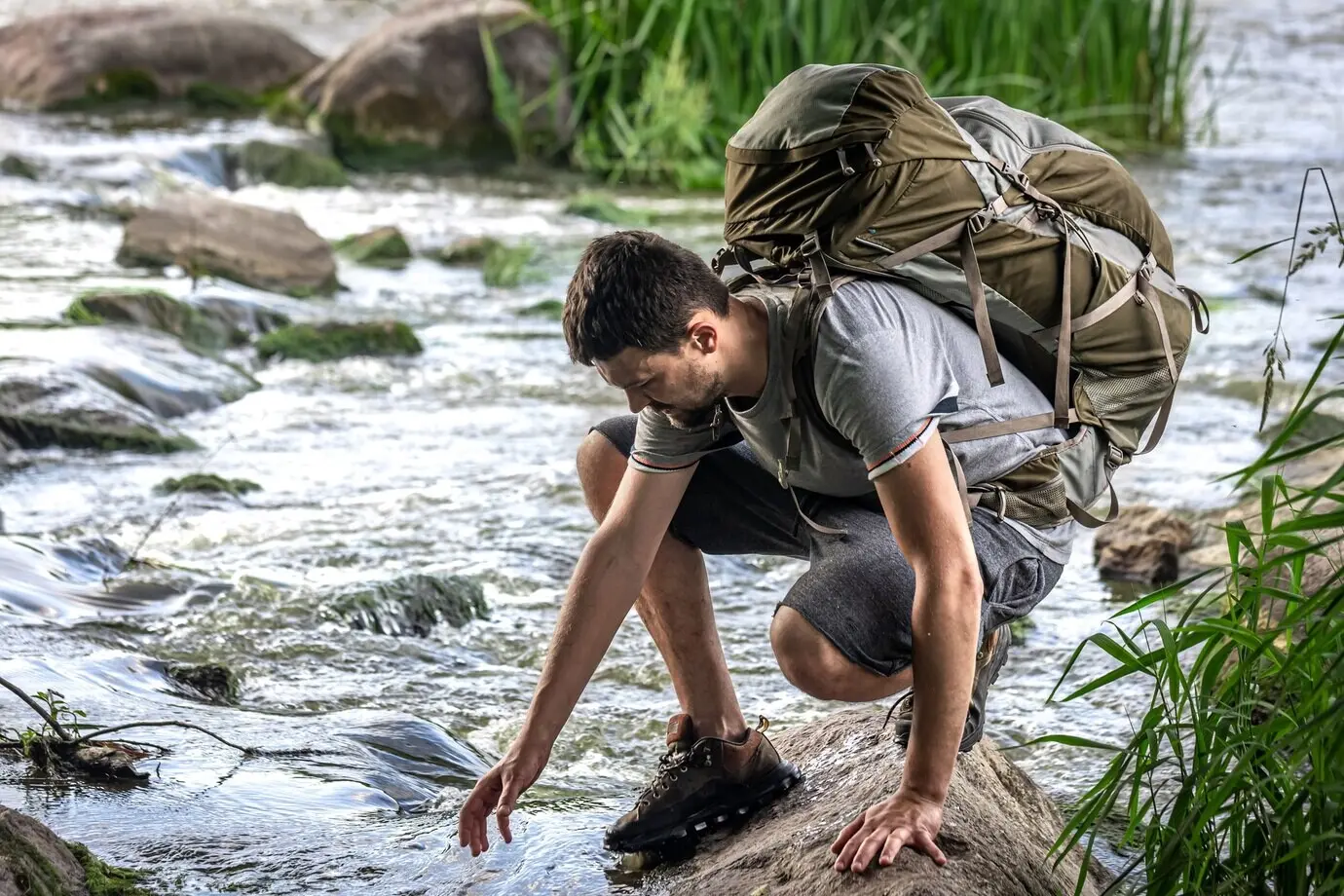 Ein Tourist mit großem Wanderrucksack kühlt sich in der Nähe eines Gebirgsflusses in der Sommerhitze ab.